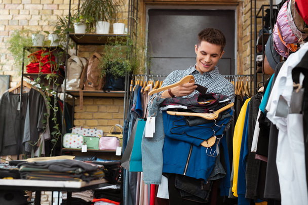 Positive young man smiling and holding big amount of clothes on hangers - Foto, immagini