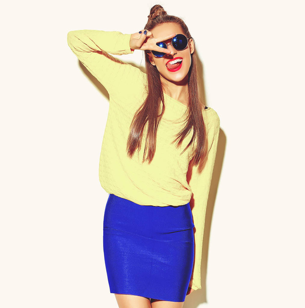 красивая счастливая милая улыбающаяся брюнетка девушка в случайных красочных хипстер желтая летняя одежда с красными губами изолированы на белом показывая знак мира и ее язык
 - Фото, изображение