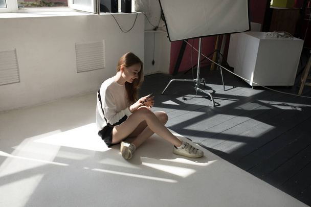 Model sits on the floor and uses a smartphone in a professional photo studio. - Photo, Image