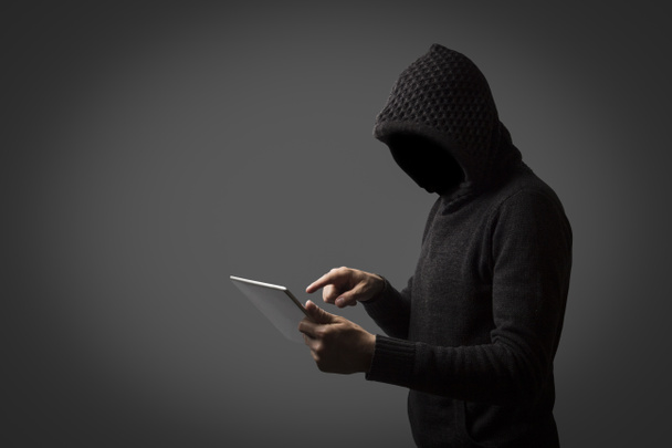 Człowiek bez twarzy w Bluza z kapturem posiada tablet w jego ręce na ciemnym tle. Koncepcja hacking danych użytkownika. Posiekany blokady, karta kredytowa, Chmura, e-mail, hasła, pliki osobiste - Zdjęcie, obraz
