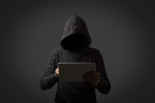 Hombre sin rostro en una sudadera con capucha sostiene una tableta en sus manos sobre un fondo oscuro. Concepto de hackeo de datos de usuarios. Cerradura hackeada, tarjeta de crédito, nube, correo electrónico, contraseñas, archivos personales
 - Foto, imagen