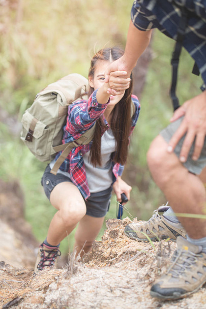 Man help pull a woman's hand in hiking activities on the mountain, teamwork and hiking concept. - Photo, Image