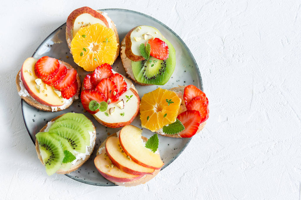 Fruit dessert sandwiches with ricotta cheese. Delicious healthy breakfast toasts with cream cheese, fresh organic fruits and berries, herbs, nuts and bee pollen. Diet healthy food, breakfast, snack. - Foto, Bild