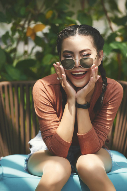 Joyful laughing young woman in sunglasses sitting outdoors - Photo, Image