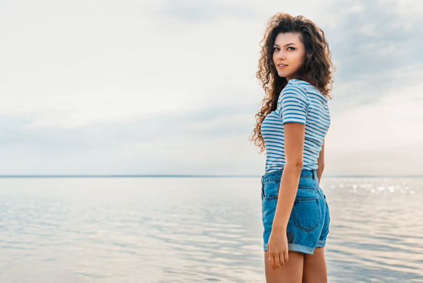 atractiva chica rizada en ropa casual posando cerca de los mares
  - Foto, Imagen