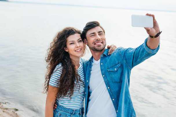 young smiling couple taking selfie on smartphone near sea - Photo, Image
