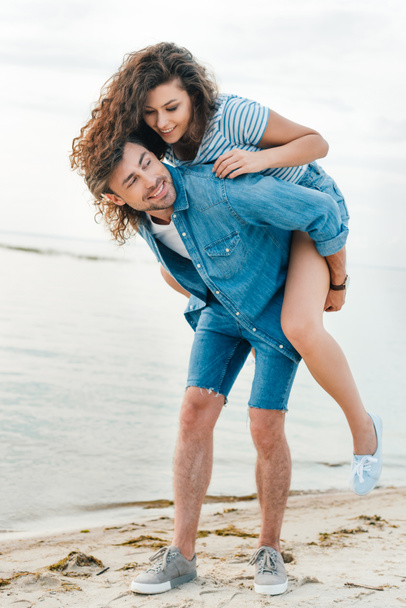 happy boyfriend giving piggyback for his girlfriend on seashore - Photo, Image