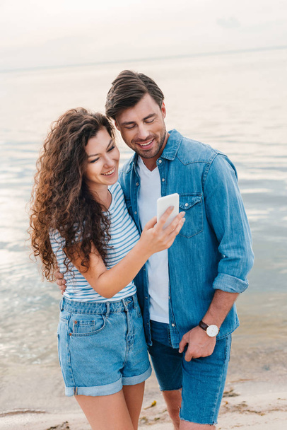 young smiling couple using smartphone near sea   - Фото, зображення