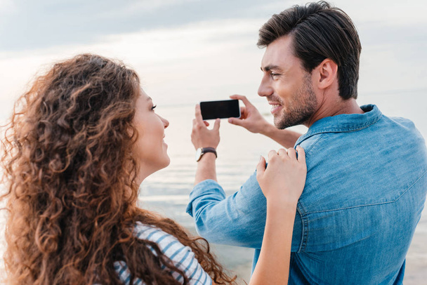 smiling couple taking photo of sea on smartphone   - Foto, Bild