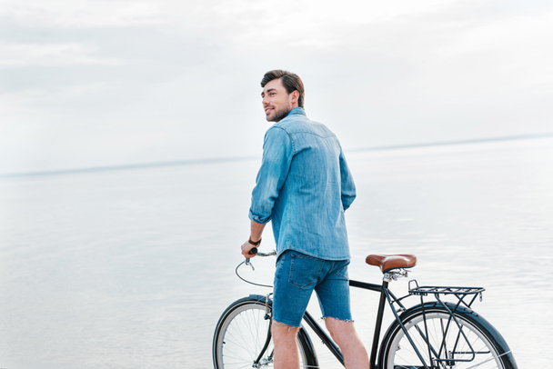 komea mies kävelee polkupyörän kanssa lähellä merta
 - Valokuva, kuva