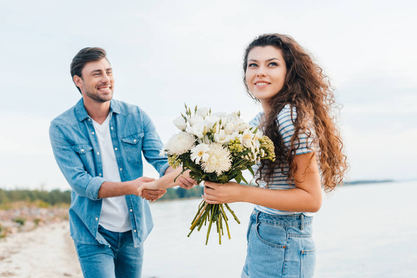 young girlfriend with bouquet holding hands with boyfriend - Φωτογραφία, εικόνα
