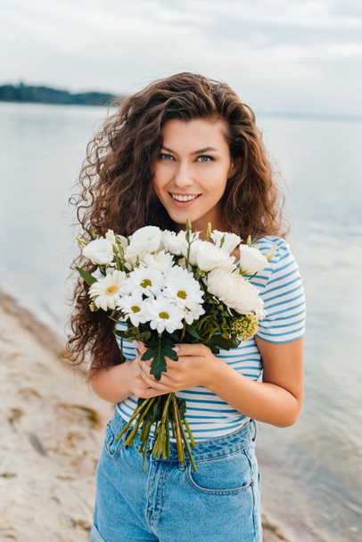 attractive happy woman posing with bouquet of flowers on beach - Zdjęcie, obraz
