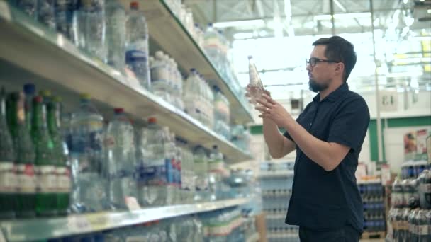 Ο άνθρωπος πελάτης παίρνει δύο μπουκάλια με νερό από το ράφι και ανάγνωση - Πλάνα, βίντεο