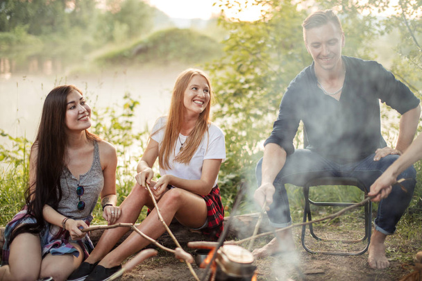 cheerful girls and pleasant boy are cooking on bonfire - Photo, image