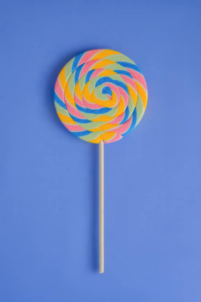 A multicolored round lollipop on a bright blue background.  - 写真・画像