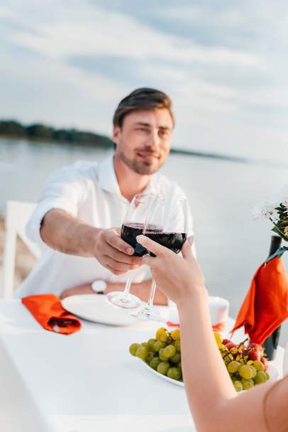 couple clinking with wineglasses during romantic date on seashore - Foto, imagen