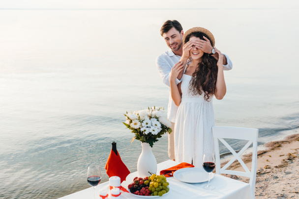 hombre feliz cerrando los ojos y haciendo sorpresa para la novia, cita romántica cerca del mar
 - Foto, Imagen