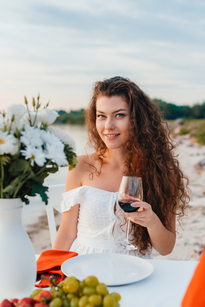 Atrakcyjna dziewczyna uśmiechający się trzyma kieliszek na romantyczną randkę na plaży - Zdjęcie, obraz