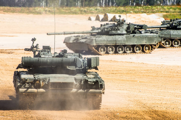 Военный танк едет через поле, на заднем плане два других танка
 - Фото, изображение
