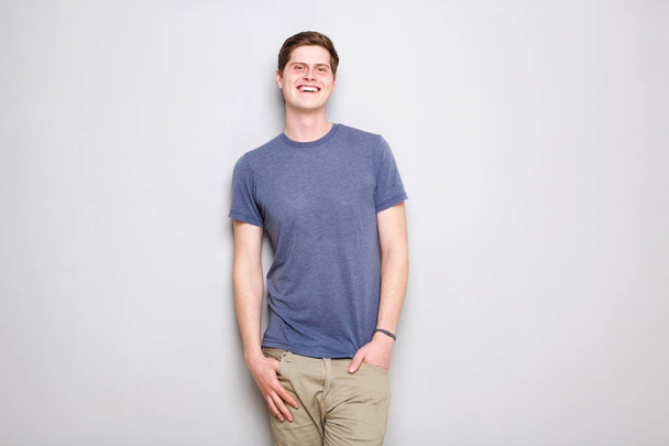 Портрет улыбающегося молодого человека, стоящего у серой стены
 - Фото, изображение