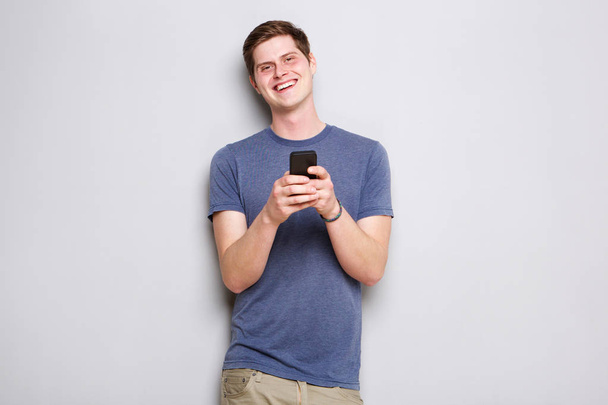 Retrato de joven feliz de pie junto a la pared con teléfono móvil
 - Foto, imagen