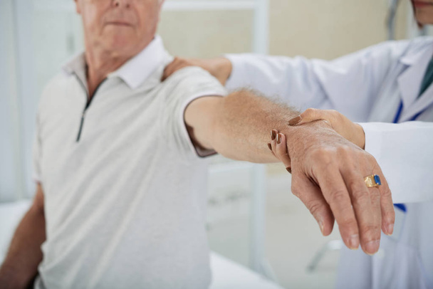 Обрезанное изображение врача, осматривающего руку пациента после реабилитации
 - Фото, изображение