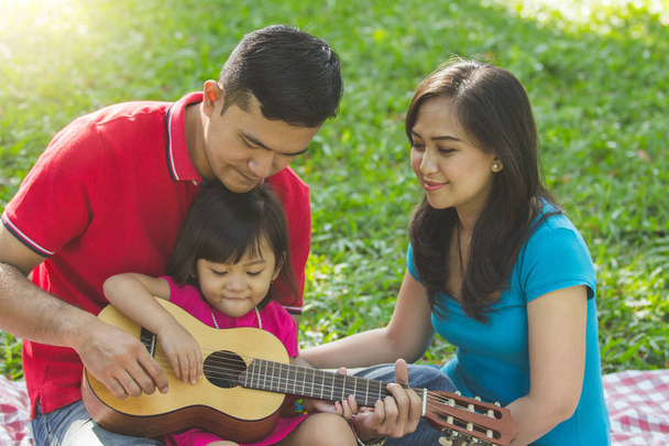 Dad teaching her little daughter to play guitar while mom watching - Foto, Imagen