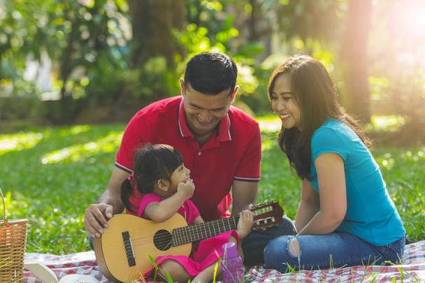 Táta a máma a její roztomilá malá dcera hrát hudbu v parku - Fotografie, Obrázek