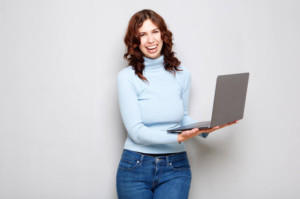 Portré, fiatal nő, nevetve és a gazdaság laptop számítógép, sötétszürke háttérrel - Fotó, kép