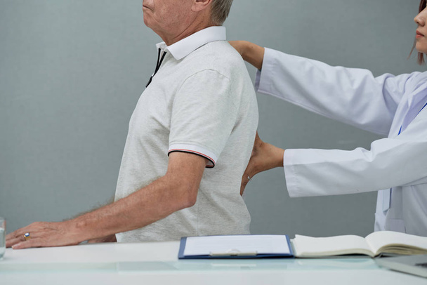 Bijgesneden afbeelding van senior man met zijn rug onderzocht in medische kantoor - Foto, afbeelding