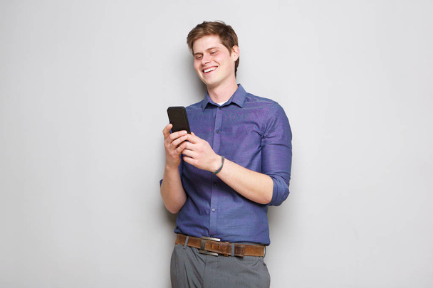 Retrato de jovem feliz em pé por parede cinza com telefone celular
 - Foto, Imagem