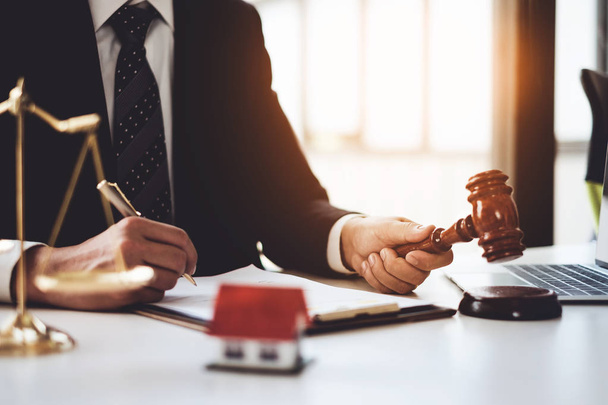Lawyer in the office with brass scale and writing in contract on wooden table. Justice, law, property and real estate concept. - Фото, зображення