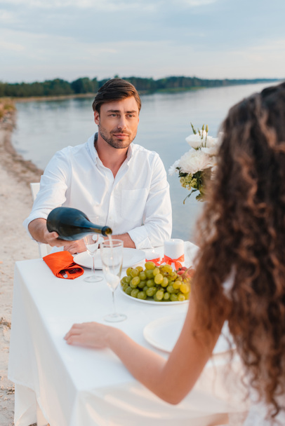 man gieten champagne voor vriendin tijdens romantische datum op strand - Foto, afbeelding
