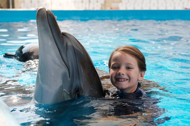Kid ja Dolphin. Tyttö ui ja halaa pullonokkadelfiiniä sinisessä vedessä. Delfiini avusteinen hoito
 - Valokuva, kuva
