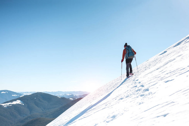 Człowiek wspina się na szczyt góry. Góral w snow buty nosić plecak. Podróż w góry zimą. Ekstremalne wakacje w przyrodzie. Turystycznych w ekstremalnych warunkach. - Zdjęcie, obraz