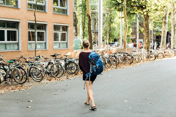 Κορίτσι φοιτητής ή τουριστική διασχίζει το δρόμο και πηγαίνει προς το χώρο στάθμευσης ποδηλάτων - Φωτογραφία, εικόνα