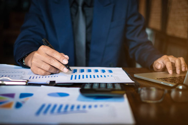 Close up Businessman consultant holding pen and pointing at financial on wooden desk in coffee shop. freelance, tax, accounting, statistics and analytic research concept. - Photo, Image