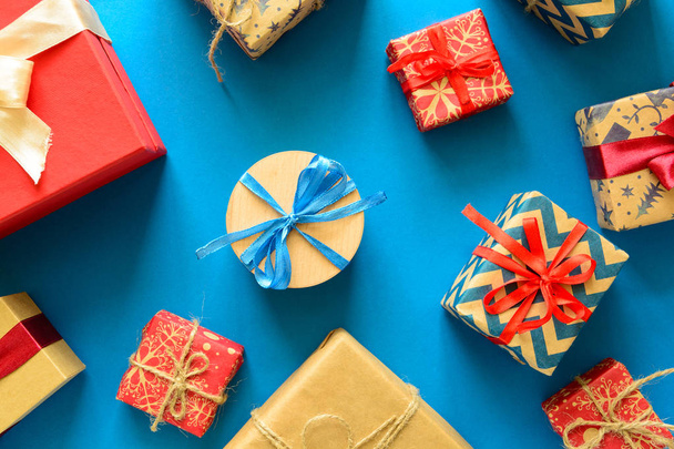 Top view on Christmas gifts wrapped in gift paper decorated with ribbon on blue paper background. New Year, holidays and celebration decorations concept. Copy space. Flat lay - Zdjęcie, obraz
