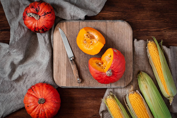Sliced and whole pumpkins, corn on cutting board with knife on wooden background with canvas fabric. Top view still life with autumn harvest in rustic style. - Fotografie, Obrázek