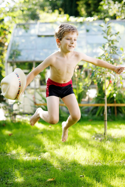 Милий активний хлопчик стрибає в саду в теплий сонячний літній день. Щаслива дитина дивиться на камеру. Чарівна дитина з світлим волоссям і блакитними очима
 - Фото, зображення