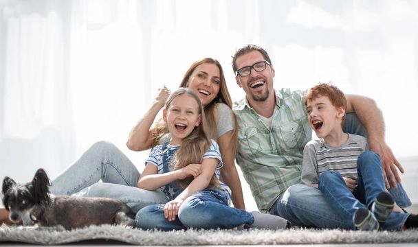 cheerful family sitting on the carpet in the new living room - Foto, Bild