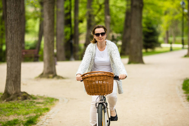 Adult woman in casual wear riding female bicycle in spring park - Foto, Bild