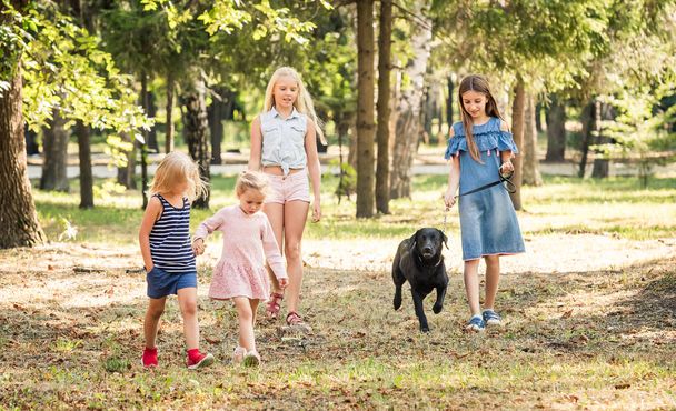 Little girls walking with a black dog in a park - Fotó, kép