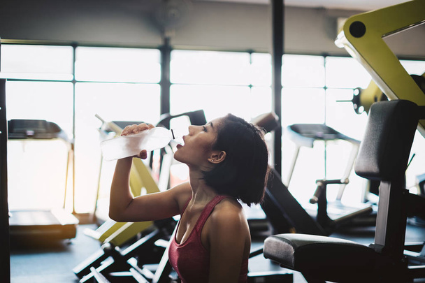 Привлекательная фитнес-женщина расслабляется и пьет воду после тренировки в тренажерном зале. Портретный спорт и здоровая концепция
. - Фото, изображение