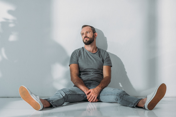 full length view of depressive bearded middle aged man sitting on floor and looking away  - Photo, Image