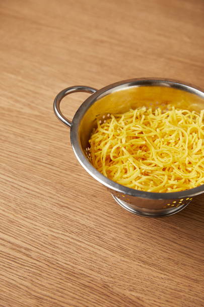 Hochwinkelblick auf Metallsieb mit Spaghetti auf Holztisch - Foto, Bild