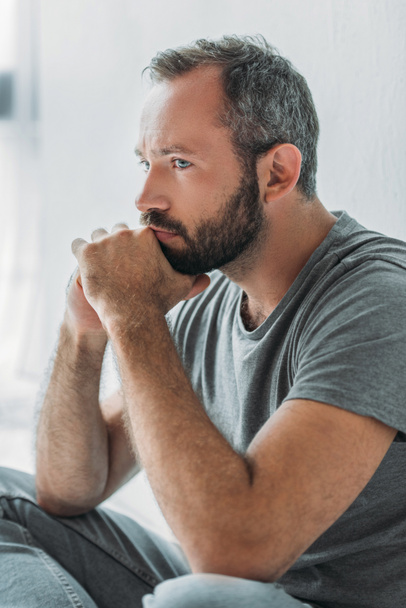 sad handsome bearded man sitting with hands on chin and looking away - Foto, Imagem