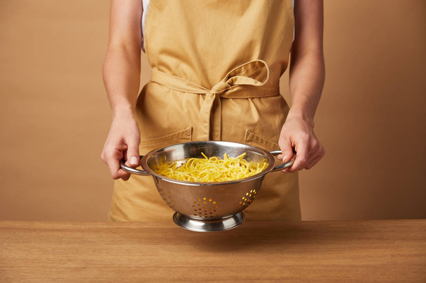 bijgesneden schot van vrouw in gele schort holding vergiet met spaghetti - Foto, afbeelding