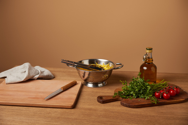 espaguetis en colador de metal con verduras y aceite de oliva sobre mesa de madera
 - Foto, imagen