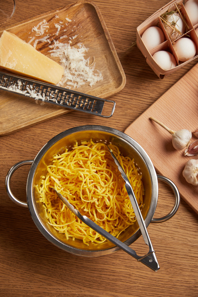 top view of spaghetti in metal colander surrounded with ingredients for pasta on wooden table - 写真・画像